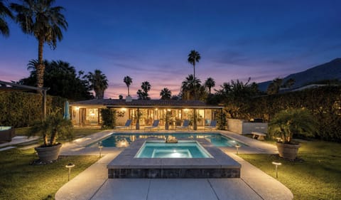 A stunning resort-style property featuring a sparkling pool and spa set among lush gardens with mountain views, ideal for evening relaxation under swaying palms.