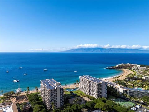 A stunning aerial view of the beachfront property nestled along pristine shores, with neighboring islands visible across the deep blue Pacific. The resort features modern buildings, tropical landscaping, and beach access.
