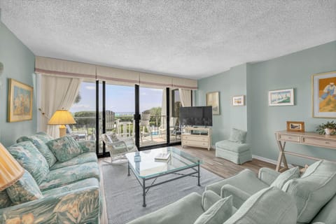 Settle into your calming coastal retreat with soothing blue-green tones, comfortable seating, and a private balcony overlooking lush grounds and the pool area—your perfect spot to unwind.