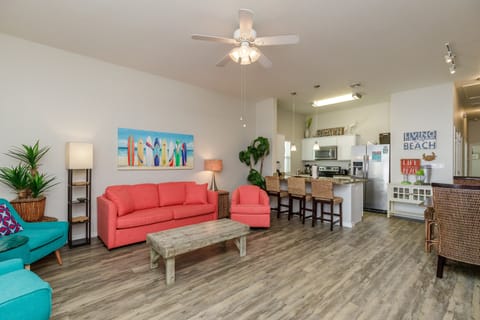 Relax in your bright, coastal living space featuring vibrant coral seating and beach-themed decor that flows into a modern kitchen.