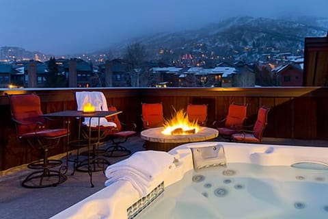 Unwind in your private hot tub while flames dance in the fire pit, surrounded by twinkling mountain lights at dusk.