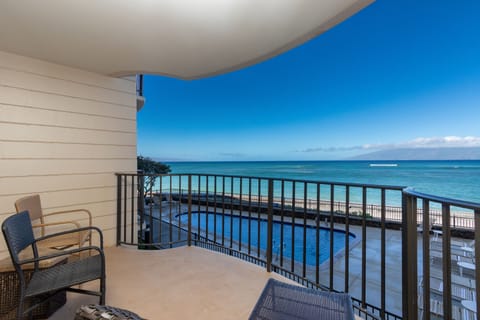 A covered terrace showcasing panoramic ocean views, with a poolside deck below and tranquil turquoise waters stretching to the horizon under clear blue skies.