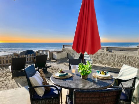 Beachfront terrace offers stunning ocean views with dining setup overlooking sandy shores and waves at sunset.