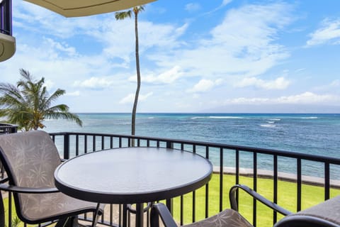 Oceanfront balcony offering stunning sea views framed by swaying palms. Enjoy morning coffee at your private table as waves roll in beneath clear blue skies.