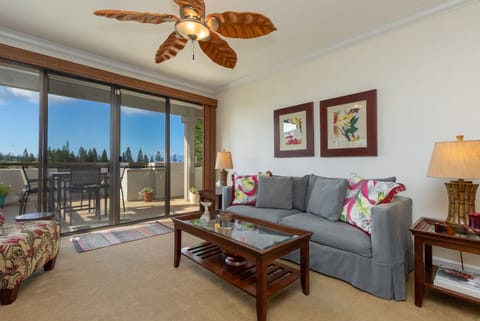 Unwind in your inviting living room with comfortable seating, tropical decor, and a breezy ceiling fan. Step onto your private balcony to enjoy views of surrounding greenery.