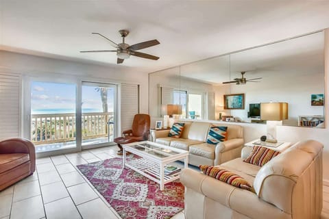 - Spacious living room with ocean views through sliding glass doors inviting natural light inside  
- Comfortable seating, large mirror wall, and cozy décor perfect for family gatherings  
- Ceiling fan, flat-screen TV, and beach-inspired style creat