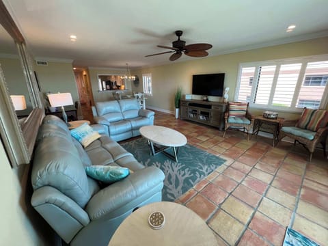 - Spacious living room with plush leather sofas and flat screen TV for comfort  
- Ceiling fan and large windows brighten the space with natural light  
- Open layout connects seamlessly to dining and kitchen areas
