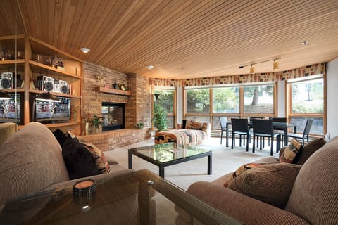 Cozy up in this warm living space with stunning wood ceiling, crackling fireplace, and peaceful garden views through floor-to-ceiling windows.