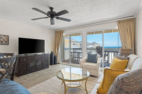 Relax in your bright living space with ocean views, where golden curtains frame the sea and comfortable seating awaits your evening unwind.
