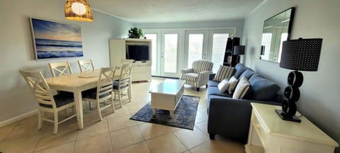 Your bright, open-plan living space blends comfort and coastal charm with plush seating, dining for six, and natural light streaming through glass doors.