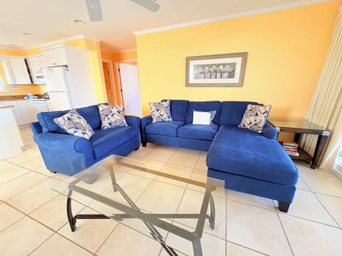 Relax in your sunny living space with plush navy sofas and modern glass table, perfect for vacation conversations.