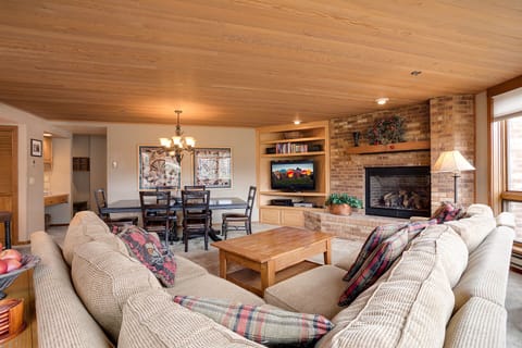Unwind in your cozy living room with stone fireplace, built-in entertainment center, and plaid-accented furnishings creating the perfect mountain retreat atmosphere.