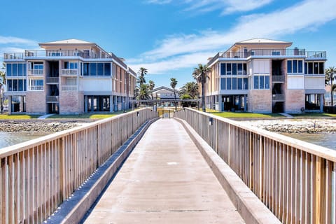 Modern beachfront buildings frame a private walkway leading to pristine waters under endless blue skies.
