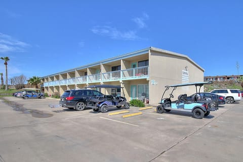 Two-story beige property building with white balconies and ample parking including golf carts, perfect for easy arrivals.
