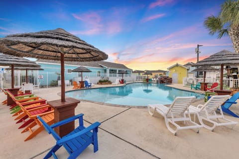 Dive into crystal-clear waters while colorful loungers and thatched umbrellas create your perfect poolside paradise under painted skies.