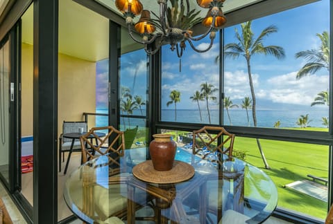 Gather around this elegant glass dining table beneath a statement chandelier, framed by sweeping ocean and palm tree views that bring the beauty of paradise right to your table.