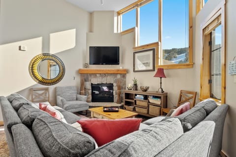 Relax in your cozy living room with warm fireplace, plush seating, and stunning mountain views through bright windows.