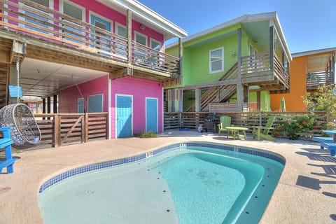 Colorful beach house complex featuring vibrant pink, green, and orange buildings surrounding a sparkling shared pool area with modern balconies and coastal charm.