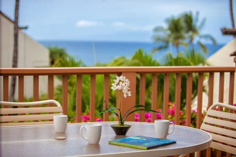 Tropical ocean-view balcony with outdoor seating, palm trees, and coastal scenery. A serene arrival setting with distant sea and resort architecture in the surrounding area.