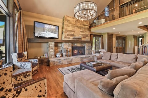 Sink into plush seating by the stone fireplace, where your evenings unfold with warmth, elegance, and mountain charm beneath a stunning chandelier.