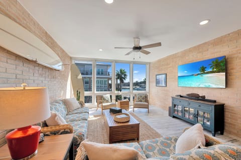 Relax in your bright living space with exposed brick walls, ceiling fan, and tropical beach scenes on the large TV.
