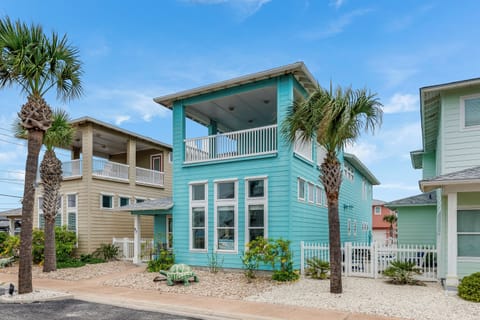 Charming turquoise beach house with covered porch surrounded by swaying palm trees in a coastal community.