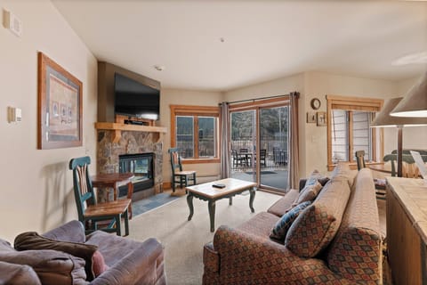 Cozy mountain retreat living room with stone fireplace, plush seating, and balcony access for your perfect alpine getaway.