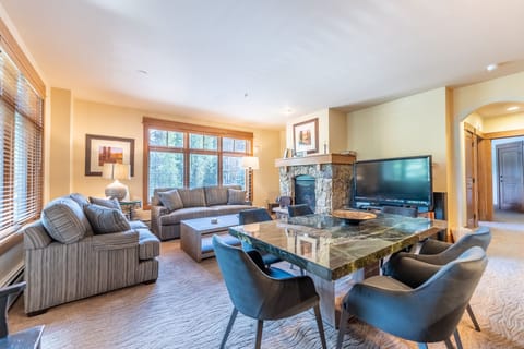 Unwind in your spacious living room featuring plush sofas, a cozy stone fireplace, and modern amenities for the perfect mountain retreat.
