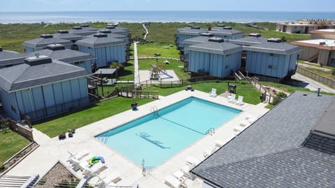Aerial view of a beachfront resort complex featuring modern vacation homes surrounding a central pool area, just steps from the ocean.