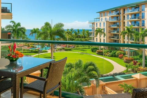 Scenic lanai dining with lush resort landscaping, mountain-lined horizon, and distant ocean sparkle.