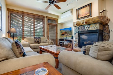 Unwind in your cozy living room where rustic stone fireplace meets plush seating, perfect for evenings watching TV or gazing through wood blinds.