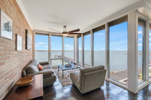 Relax in your sun-filled living room with stunning water views, exposed brick charm, and comfortable seating that invites peaceful moments.