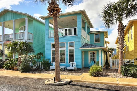 Vibrant turquoise beach house with tropical charm, surrounded by colorful coastal community and swaying palm trees.