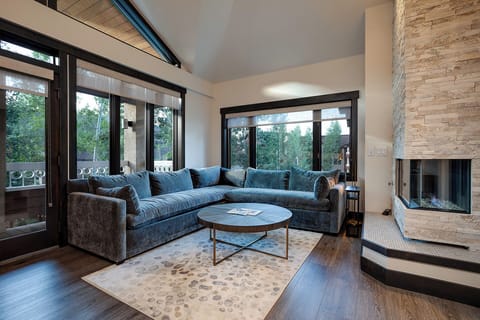 Sink into this plush sectional by your private fireplace, where floor-to-ceiling windows frame peaceful garden views for your perfect evening retreat.