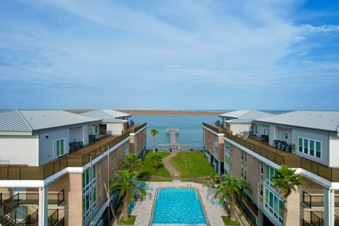 Modern beachfront resort buildings frame a pristine swimming pool area with direct ocean access and panoramic sea views.