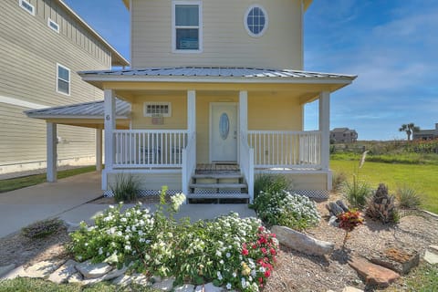 Charming coastal property entrance with covered porch and beautiful landscaped gardens featuring colorful flowers and tropical plants.