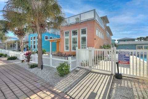 Colorful beach cottages with white picket fences and palm trees create a charming coastal village entrance.