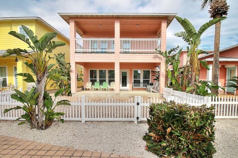 Charming coral-pink beach house with covered balcony and tropical landscaping in a colorful coastal neighborhood.