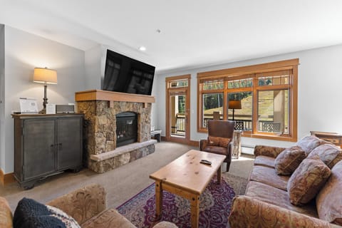 Cozy up in your spacious living room with stone fireplace, plush seating, and mountain views through expansive windows.