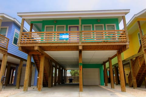 Bright green beach house elevated on sturdy wooden pillars with covered parking and coastal charm in a colorful neighborhood.