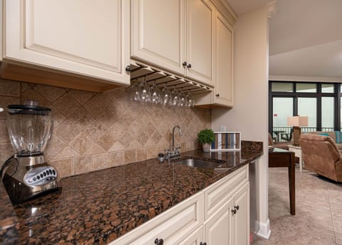 This stylish wet bar features elegant cabinetry, a granite countertop, and a cozy seating area just beyond