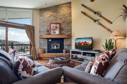 Unwind in your stylish living room with cozy furnishings, stone fireplace, and scenic mountain views from your private balcony.