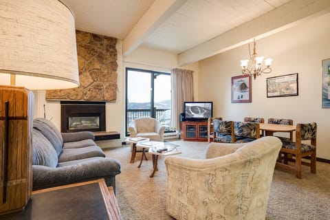 Relax in your cozy living room with stone fireplace, plush seating, and scenic mountain views through large windows.