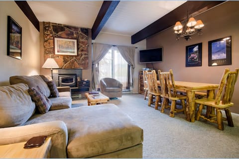 Cozy up in your rustic living space with exposed beams, stone fireplace, and handcrafted dining set for memorable mountain evenings.