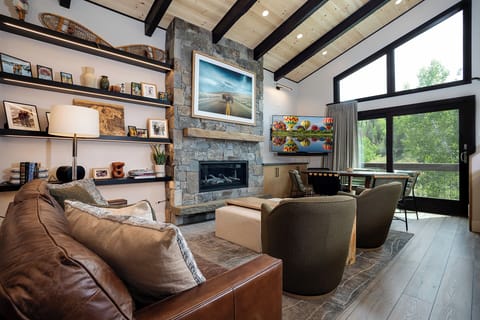 Unwind in your stylish living space with exposed beams, stone fireplace, and floor-to-ceiling windows framing forest views.