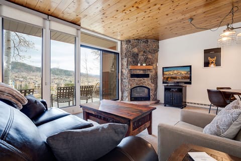 Relax in your cozy living room with stone fireplace and mountain views through expansive windows.