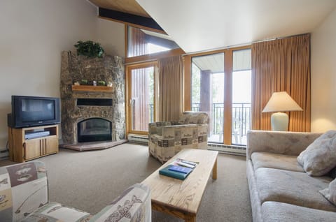 Cozy up in your comfortable living room with a crackling stone fireplace, plush seating, and mountain views through floor-to-ceiling windows.