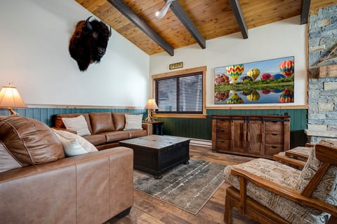 Sink into plush leather sofas beneath rustic wood beams in your cozy living room, where colorful balloon artwork brightens stone-accented walls.