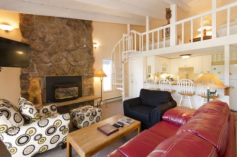 Unwind in your cozy living space featuring a stone fireplace, spiral staircase to the loft, and open kitchen—perfect for relaxing evenings.