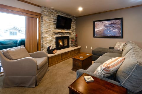 Relax in your cozy living room with crackling fireplace, plush seating, and mountain views through large windows.